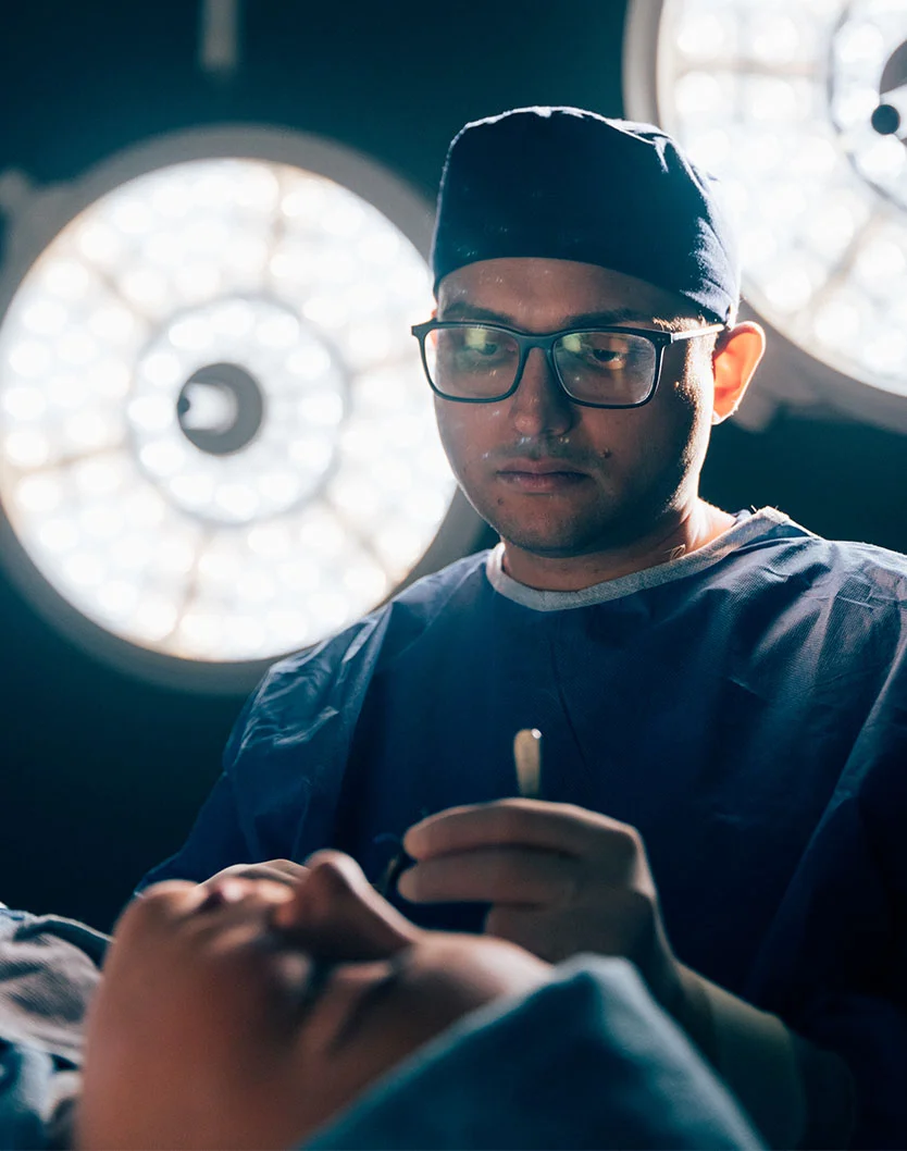 A close up shot shot of Dr. Kachare in surgery. He wears blue scrubs, hat and white gloves while he preforms with precession and focus. - Septoplasty in Greenville, NC